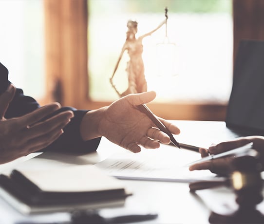 Two lawyers discuss the details of a case with a statue of Lady Justice in the background